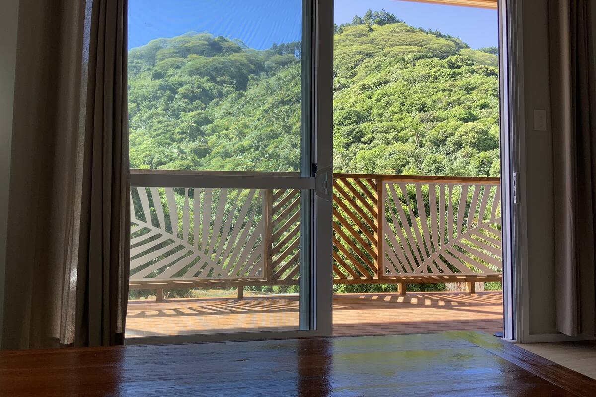 A room with a sliding glass door leading to a balcony with a view of a lush green hillside.