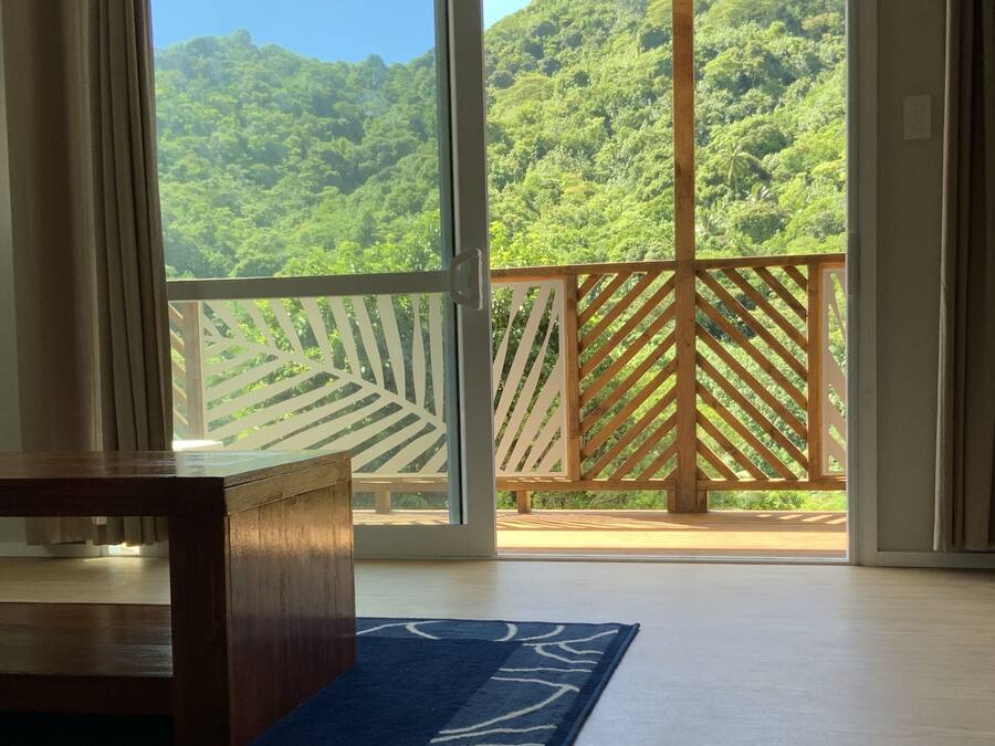 Une pièce dotée d’une grande porte-fenêtre coulissante qui donne sur un balcon offrant une vue sur une colline verdoyante.