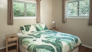A bedroom with a bed, two windows with curtains, a bedside table with a lamp, and a nightstand.
