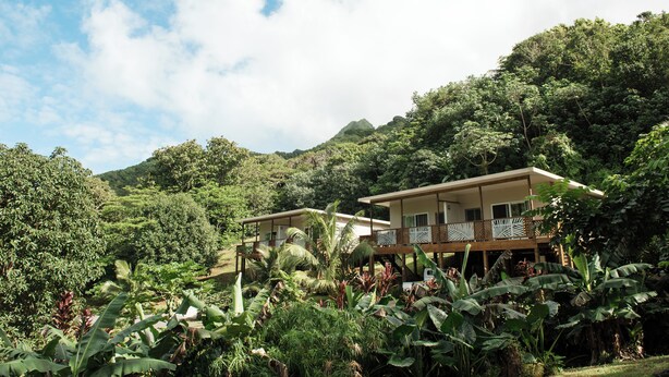 A resort with two buildings surrounded by lush greenery and a mountain in the background.