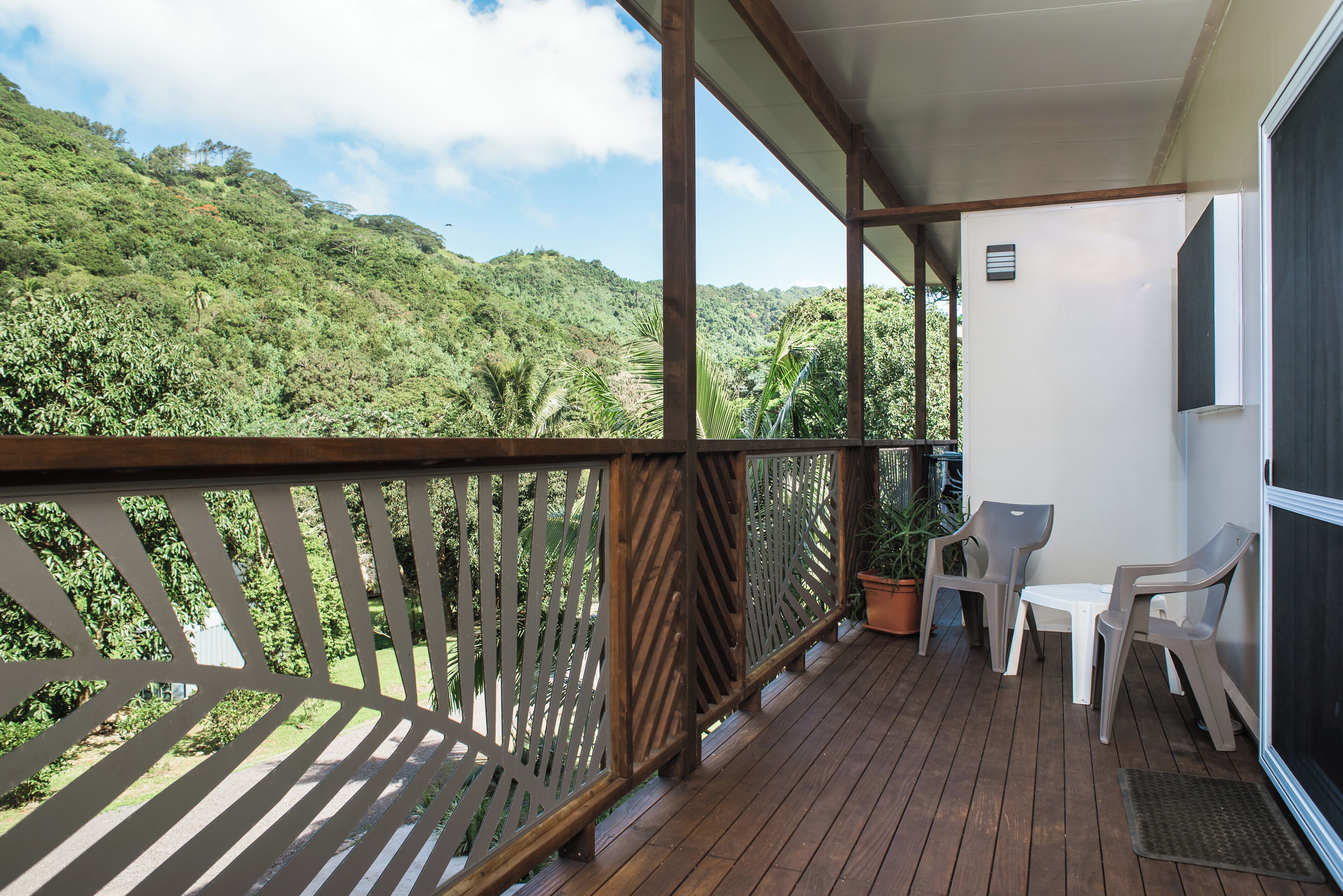 A balcony with a wooden floor, a white table, two chairs, and a potted plant.