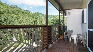A balcony with a wooden floor, a white table, two chairs, and a potted plant.
