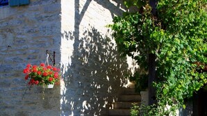 Un mur de pierre avec un portail en bois, une jardinière suspendue et un bâtiment doté d’une fenêtre et de volets.