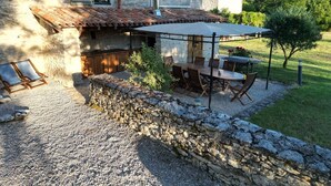 Une maison en pierre avec un toit en tuiles, un espace extérieur aménagé pour s’asseoir et un mur en pierre.