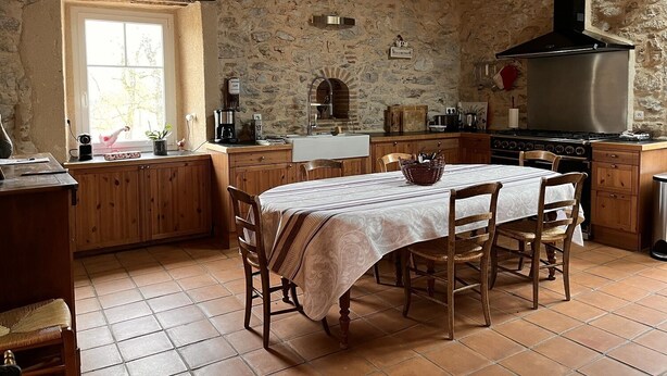 Une cuisine rustique avec un mur en pierre, des armoires en bois, une grande cuisinière et une table à manger avec des chaises.