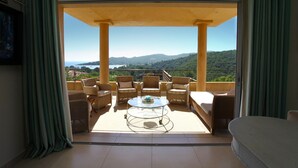 Un balcón con mobiliario de mimbre y una mesa de vidrio, con vistas a un paisaje pintoresco.