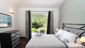 Un dormitorio con cama, mesitas de noche, cómoda y ventana con cortinas.
