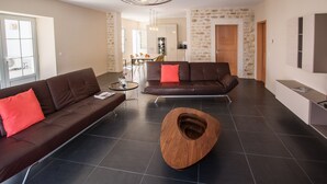 A modern living room with a brown leather sofa, a unique wooden coffee table, and a dining area in the background. - Former fisherman's house with pool in the heart of Old Cotinière (Saint-Pierre-D'oléron)