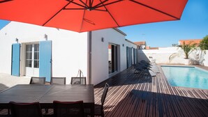 A wooden deck with a pool, a table with chairs, and a red umbrella. - Former fisherman's house with pool in the heart of Old Cotinière (Saint-Pierre-D'oléron)