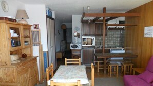 A compact kitchen with wooden cabinets, a dining table with chairs, and a purple sofa. - Holiday Apartment (Orcières)