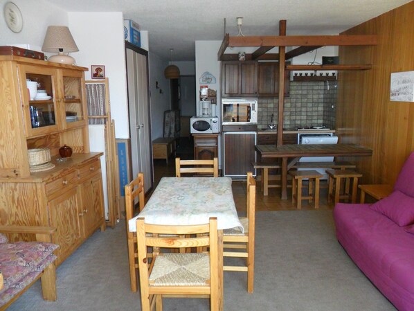 A compact kitchen with wooden cabinets, a dining table with chairs, and a purple sofa. - Holiday Apartment (Orcières)