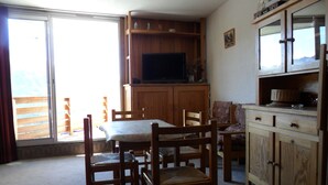 A dining area with a table and chairs, wooden cabinets, and a television. - Holiday Apartment (Orcières)