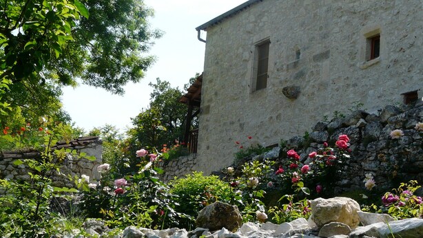 Ein rustikales Steinhaus mit Garten, der rosafarbene Rosen und eine Steinmauer zeigt.