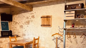 Ein rustikaler Raum mit einem Holztisch und -stühlen, einem gesteppten Teppich, einer Holzkabine mit Stauraum und einem Fernseher auf einem Regal.