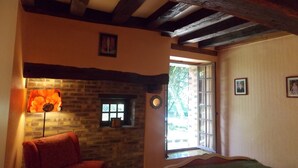 A cozy room with a brick fireplace, a wooden ceiling, and a large window. - Beautiful house in the woods on paths Colette (Saint-Sauveur-En-Puisaye)