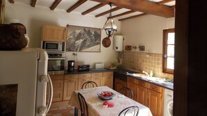 A kitchen with wooden cabinets, a microwave, a stove, and a table with a bowl of fruit. - Beautiful house in the woods on paths Colette (Saint-Sauveur-En-Puisaye)