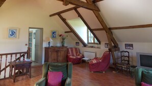 A spacious attic room with wooden beams, a wooden staircase, and a variety of seating including armchairs and a sofa. - Beautiful house in the woods on paths Colette (Saint-Sauveur-En-Puisaye)