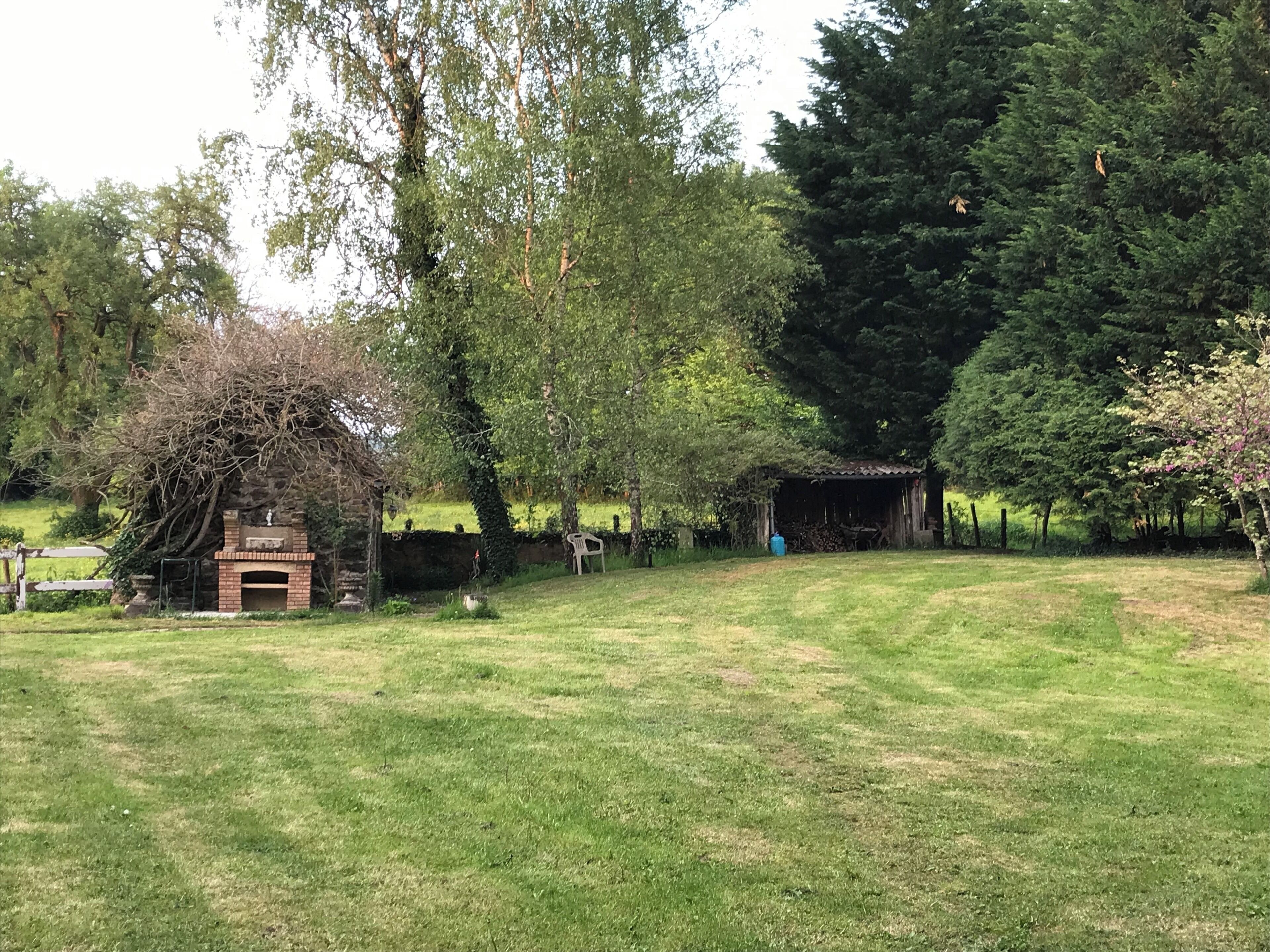 Een rustieke buitenruimte met een bakstenen gebouw, een houten tuinhuis en een grasveld.