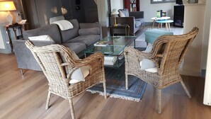 Ein modernes Wohnzimmer mit einer grauen Couch, Korbstühlen, einem Glastisch und einem Bücherregal.