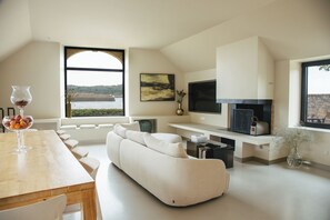 A modern living room with a sofa, a dining table with glasses, a fireplace, and a view of the outdoors.