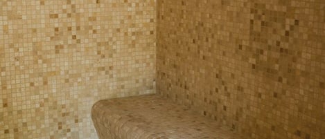 A corner of a room with a tiled wall and a curved bench.