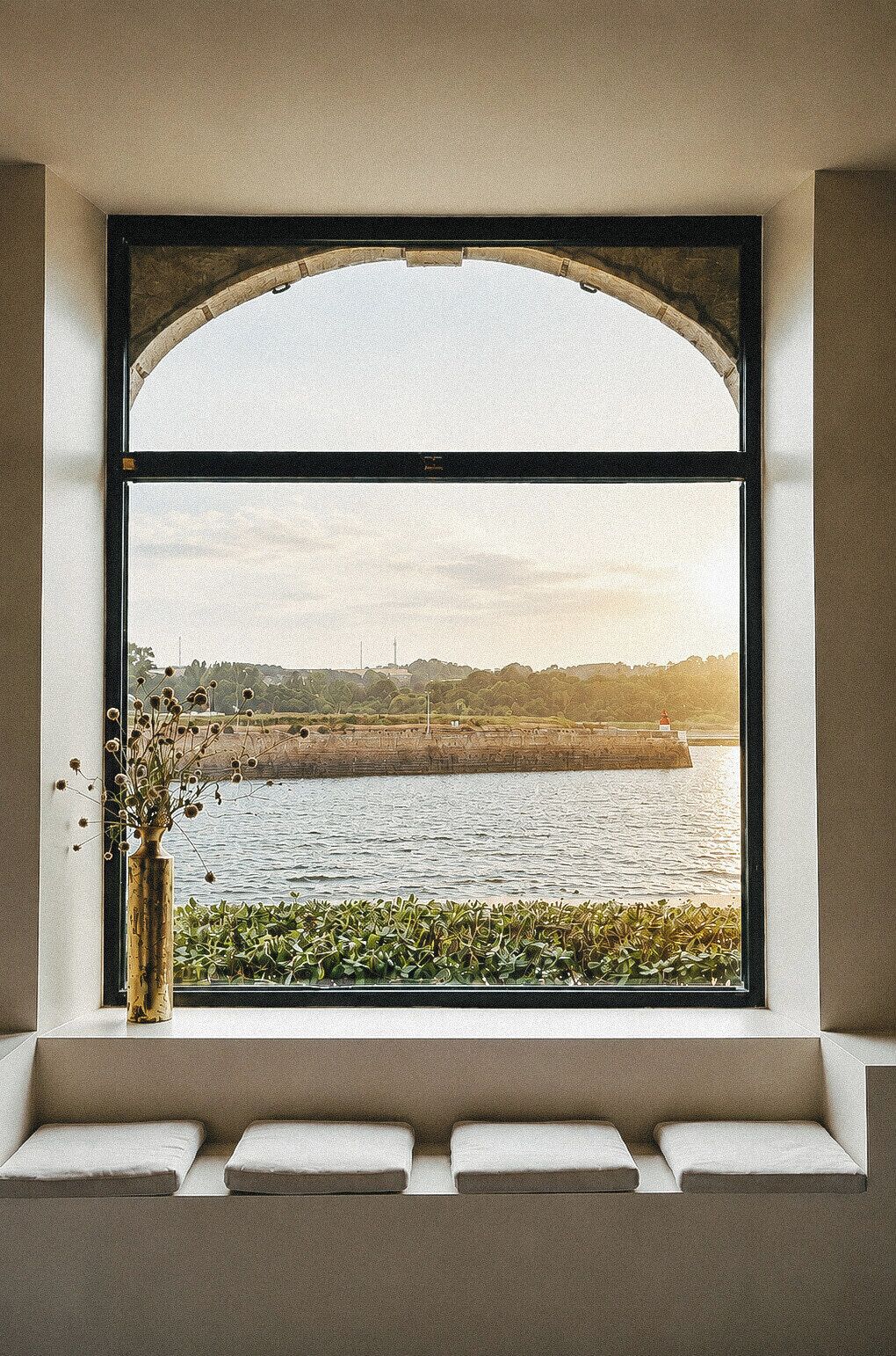 A window with a view of a body of water and a distant shoreline, framed by a simple architectural design.