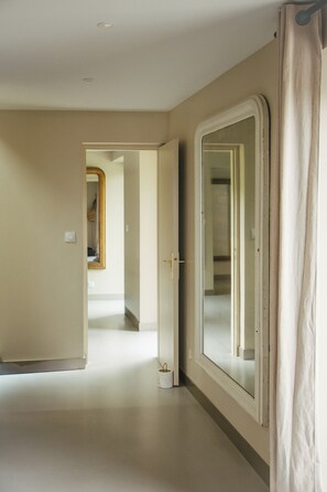 A hallway with a large mirror, a door, and a light switch on the wall.