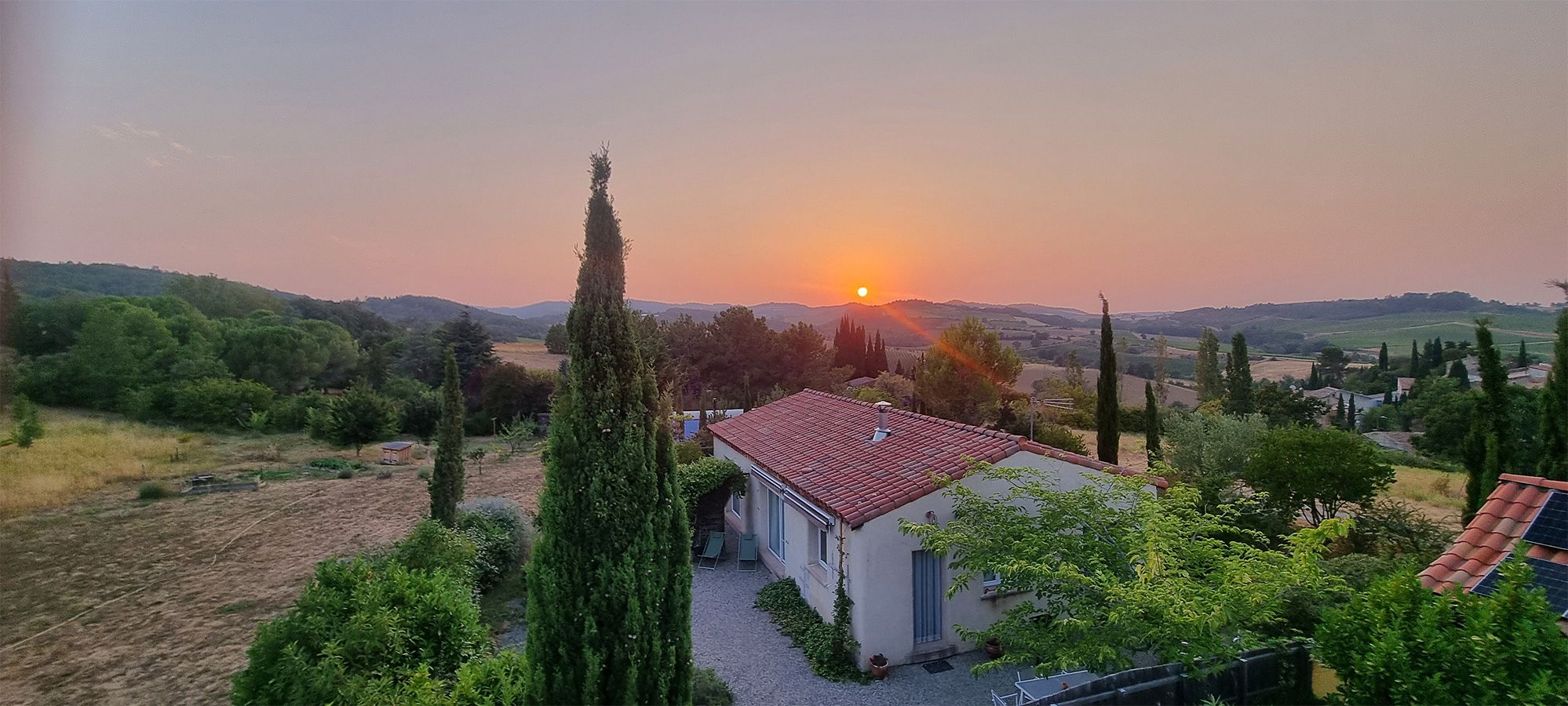 Un paysage rural avec une petite maison, un ciel dégagé et un coucher de soleil.