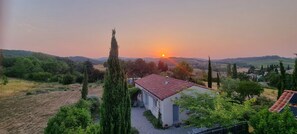 Paesaggio rurale con una piccola casa, cielo sereno e tramonto.