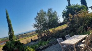 An outdoor seating area with a table and chairs, surrounded by a garden with various plants and trees, overlooking a vineyard and distant hills. - Charming villa in the heart of the hills—Discount for stays of 2 weeks or more; contact us (Donazac)