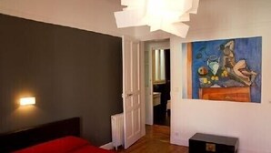 Une chambre avec un lit rouge, un radiateur blanc et un tableau accroché au mur.