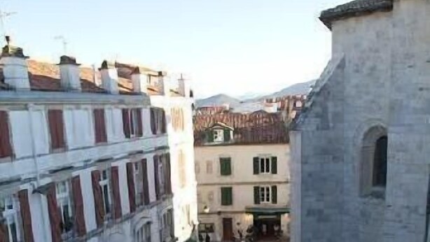 Une cour bordée de bâtiments, avec un mur de pierre et une clôture en métal.