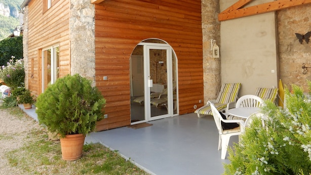 Une cabane en bois avec une façade en pierre, une véranda couverte avec des chaises et une petite fenêtre.