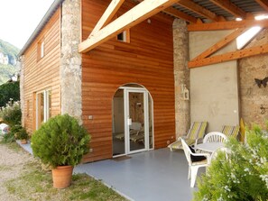 A wooden cabin with a stone exterior, a covered porch with chairs, and a small window.