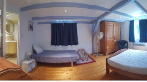 Une chambre avec deux lits, un plancher en bois, un ventilateur de plafond et une salle de bain visible à travers une porte ouverte.