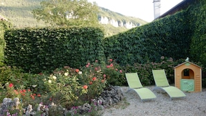 Un jardin avec une haie, une cabane et deux fauteuils de jardin.