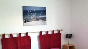 Une chambre avec deux lits simples, chacun doté d’une tête de lit rouge et d’une couvre-lit matelassée rose. On y trouve une table de chevet en bois avec une lampe, un tableau au mur et un luminaire blanc au plafond.