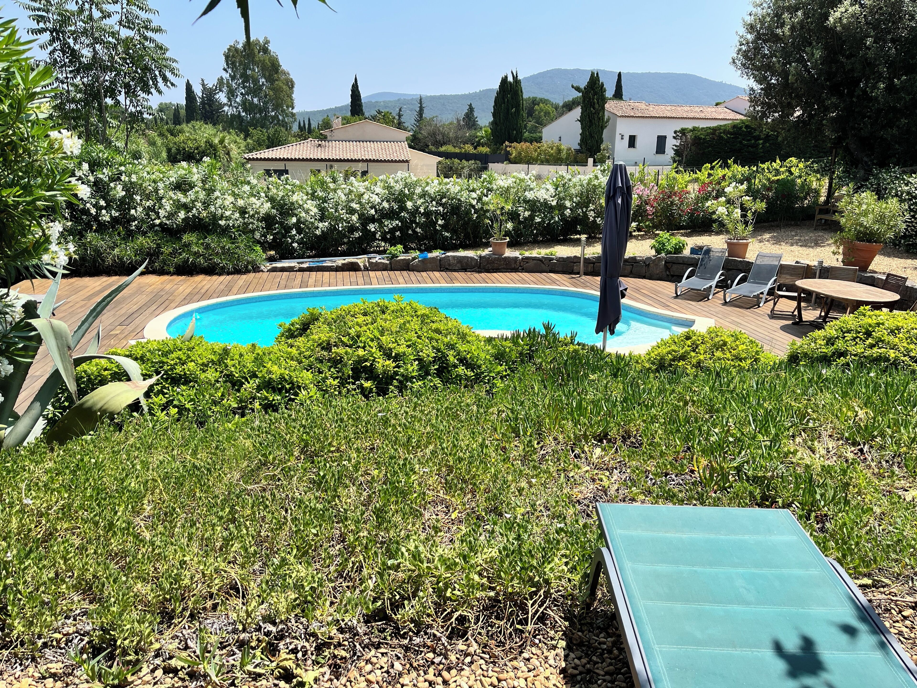 Une piscine entourée d’une végétation luxuriante, avec une terrasse aménagée comprenant des chaises longues et une table.