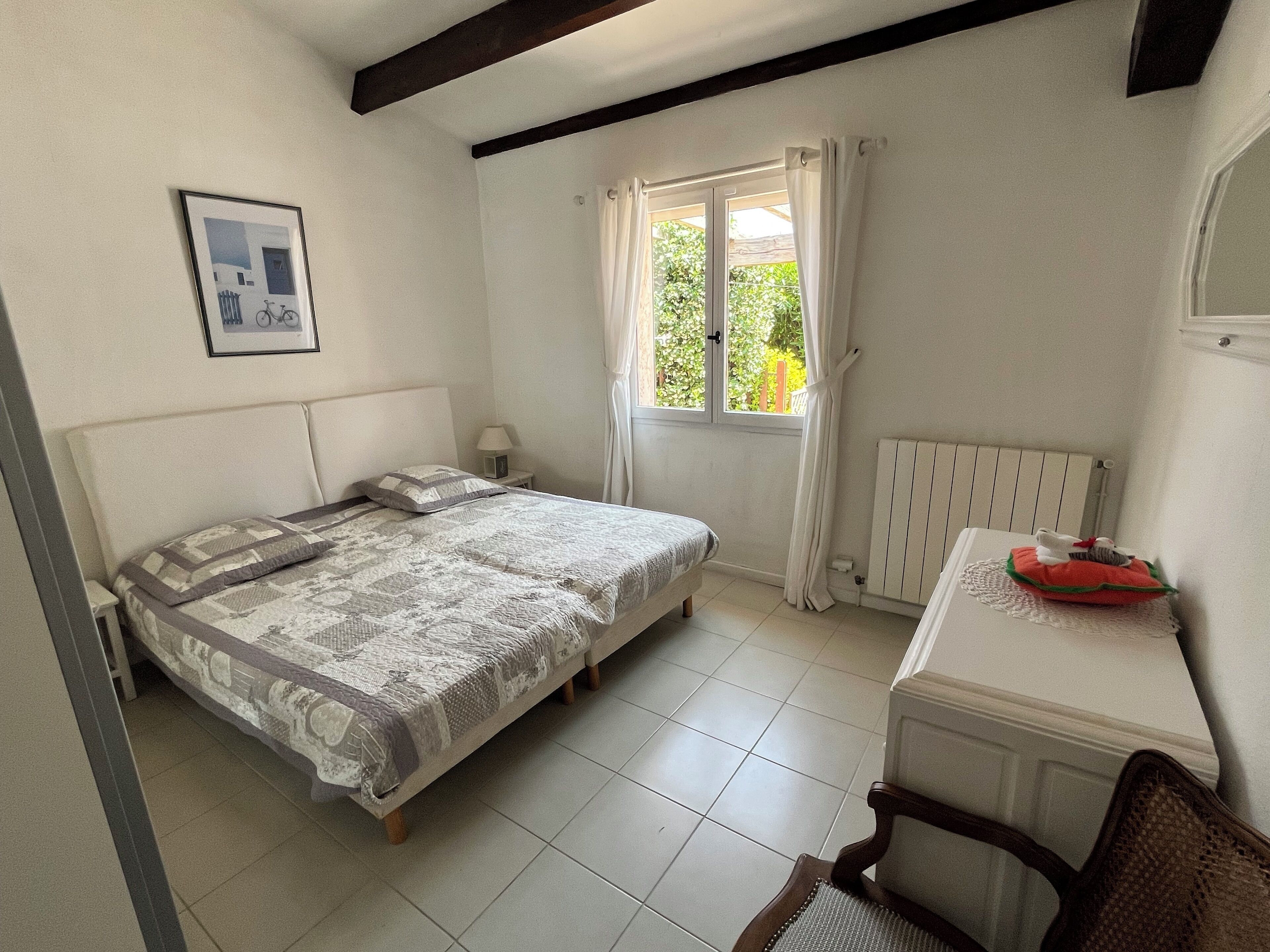 A bedroom with a bed, a desk, a chair, a radiator, and a window with curtains.