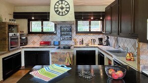 A modern kitchen with dark cabinetry, a central island, and a large wall clock. - Domaine in Provence, vinyard (Lorgues)
