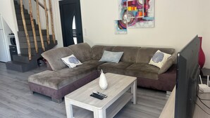 Ein modernes Wohnzimmer mit einem Ecksofa, einem Couchtisch und einem Flachbildfernseher.