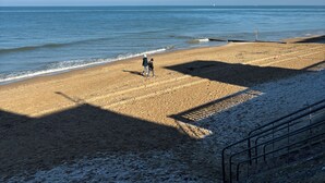 Une plage avec un ciel dégagé, un rivage sablonneux et quelques personnes qui se promènent.