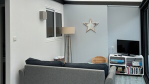 Un salon moderne avec un canapé gris, une décoration en forme d’étoile au mur, une lampe sur pied et un téléviseur posé sur un meuble blanc.