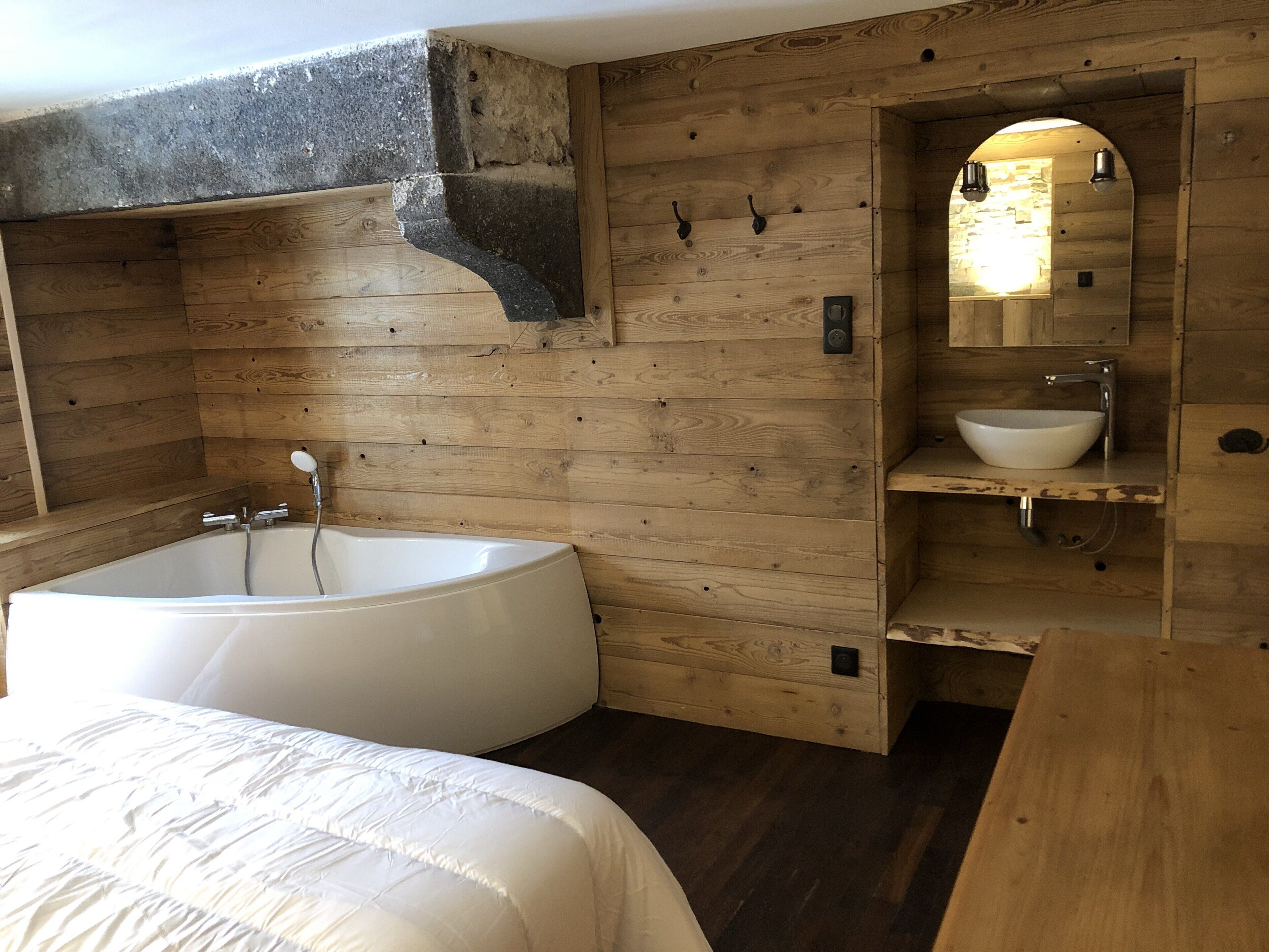 A wooden bathroom with a large bathtub, a sink, and a mirror.