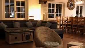 Una sala de estar acogedora con un sofá de color oscuro, una silla de mimbre, una mesa de centro de madera y un comedor con sillas y una mesa de madera.