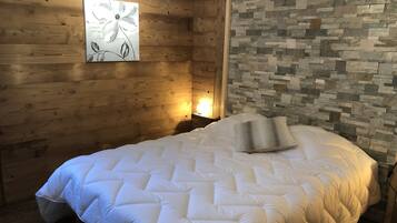 A bedroom with a wooden wall, a stone wall, a bed with white bedding, and a wall-mounted artwork.