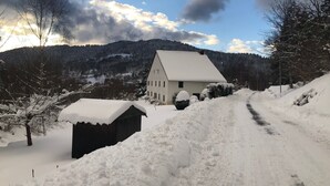 Un paisaje rural nevado con una casa blanca, un cobertizo de madera y un camino de tierra.