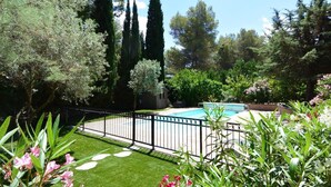 A backyard with a swimming pool, surrounded by a black metal fence, and lush greenery.