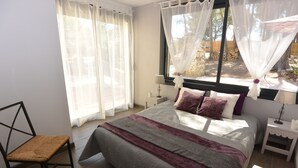 A bedroom with a bed, a chair, a nightstand, and a window with sheer curtains.