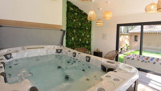 A spa area with a hot tub, wicker chairs, and a view of a garden.